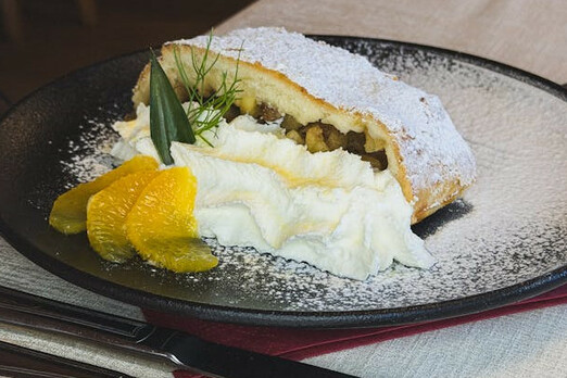 Apfelstrudel mit Puderzucker, Früchten und cremiger Füllung auf einem Teller angerichtet